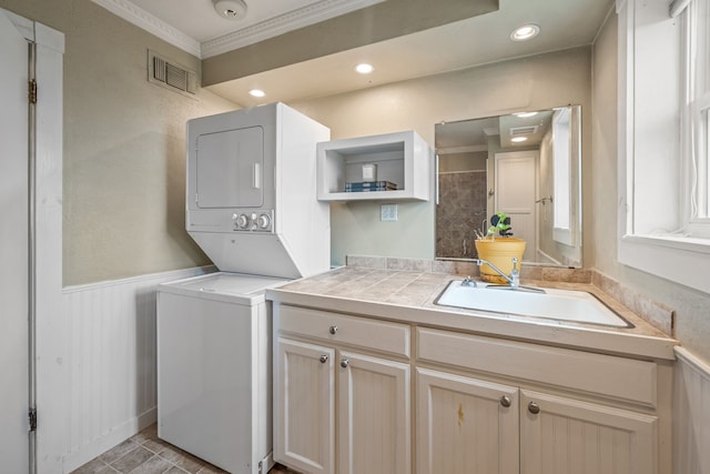 laundry area featuring stacked washer and dryer, ornamental molding, and sink