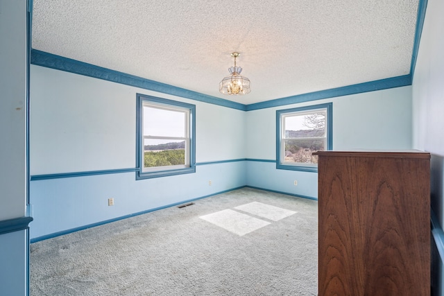 spare room with a textured ceiling, an inviting chandelier, light colored carpet, and plenty of natural light