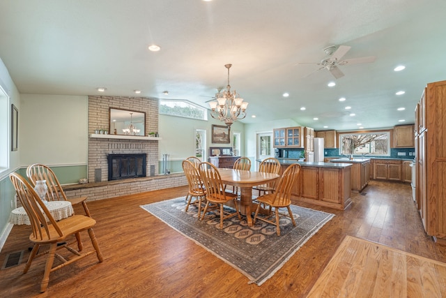 dining space featuring a fireplace, dark wood-type flooring, vaulted ceiling, and ceiling fan with notable chandelier