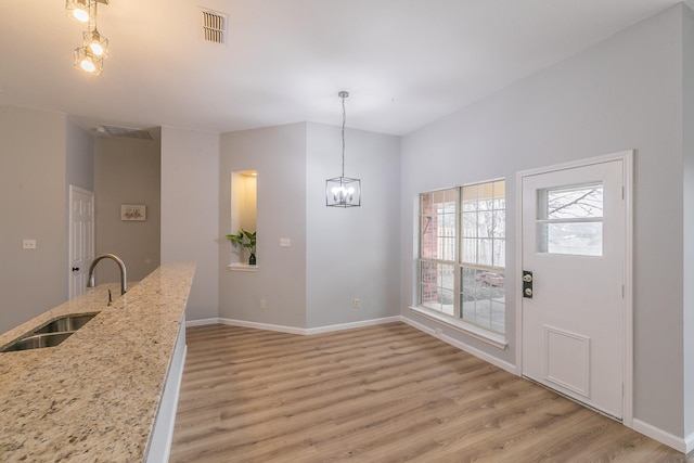 unfurnished dining area featuring sink, a chandelier, and light hardwood / wood-style flooring