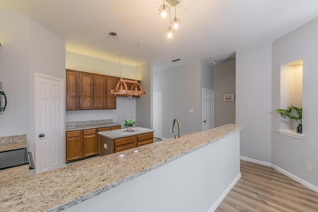 kitchen with light wood-type flooring, light stone counters, decorative light fixtures, a center island, and sink