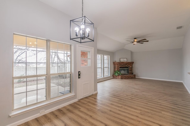 unfurnished living room featuring a brick fireplace, lofted ceiling, wood-type flooring, and ceiling fan with notable chandelier