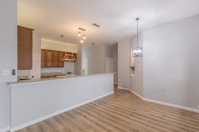 kitchen with kitchen peninsula, decorative light fixtures, light hardwood / wood-style flooring, an inviting chandelier, and light stone counters