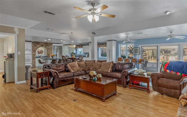 living room with light wood-type flooring and ceiling fan with notable chandelier