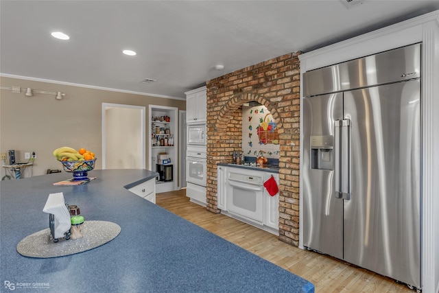 kitchen featuring ornamental molding, white cabinets, built in appliances, and light hardwood / wood-style floors