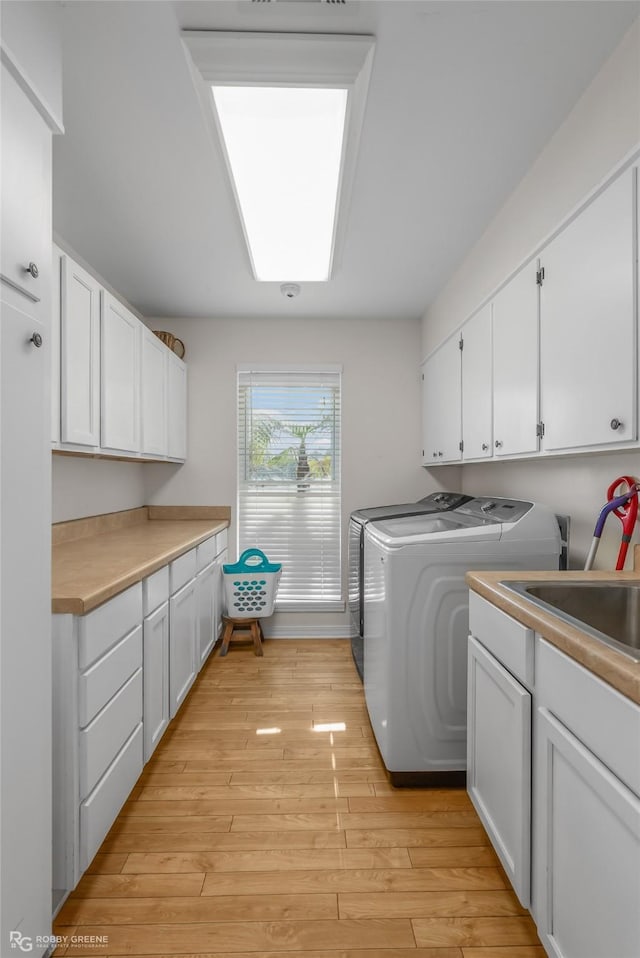 laundry room featuring cabinets, sink, light wood-type flooring, and independent washer and dryer