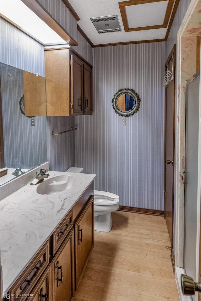 bathroom with hardwood / wood-style floors, a shower with shower door, vanity, crown molding, and toilet