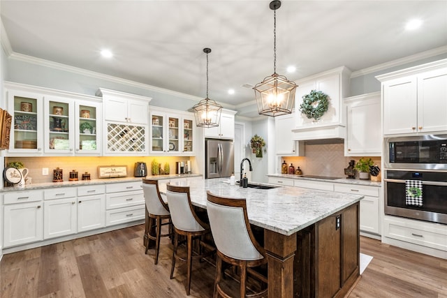 kitchen with white cabinetry, a center island with sink, appliances with stainless steel finishes, and decorative light fixtures