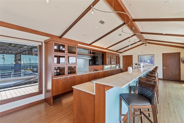 kitchen with light hardwood / wood-style floors, a breakfast bar area, a center island, and lofted ceiling with beams