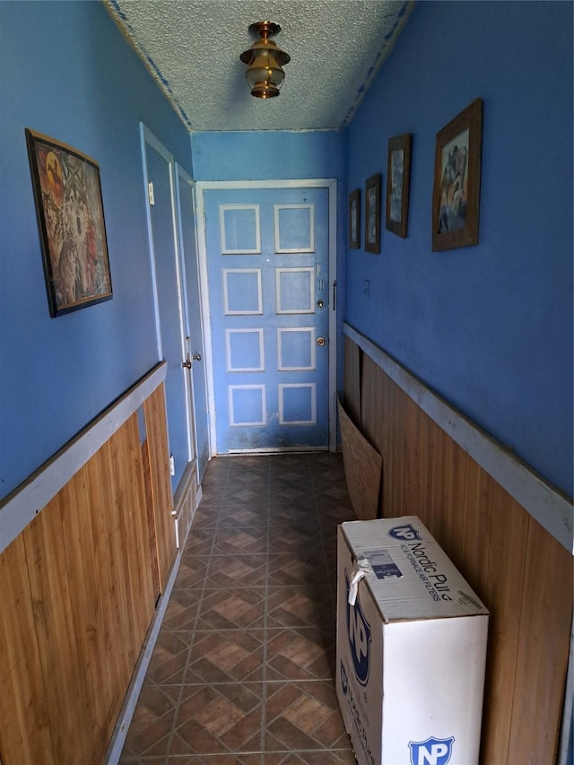 doorway with wood walls and a textured ceiling