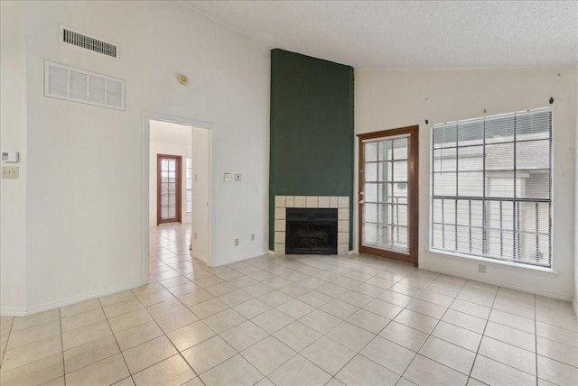 unfurnished living room featuring a textured ceiling, vaulted ceiling, a tile fireplace, and light tile patterned flooring