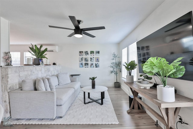 living area with ceiling fan, a wall unit AC, wood finished floors, and baseboards