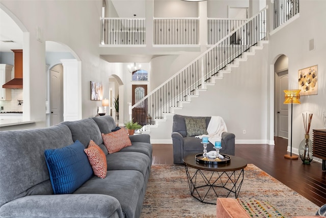 living area with arched walkways, a high ceiling, dark wood-style flooring, baseboards, and stairway