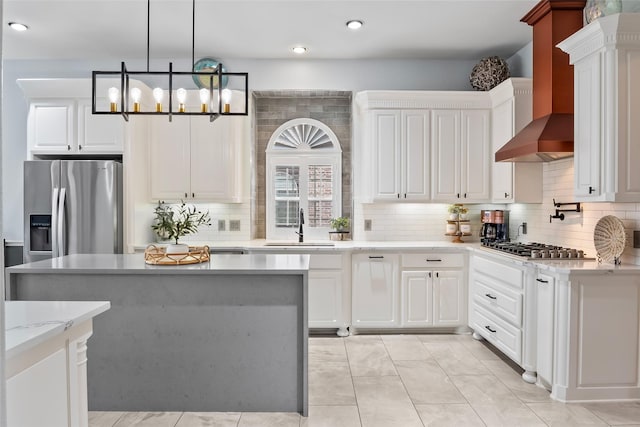 kitchen with stainless steel appliances, a sink, white cabinets, wall chimney exhaust hood, and decorative light fixtures