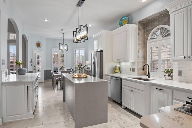 kitchen featuring decorative light fixtures, appliances with stainless steel finishes, white cabinetry, a kitchen island, and a sink