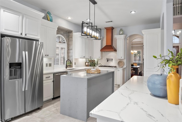 kitchen with arched walkways, white cabinets, custom range hood, a kitchen island, and stainless steel appliances