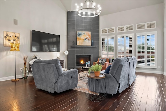 living area with baseboards, a tiled fireplace, dark wood-style floors, a high ceiling, and a notable chandelier