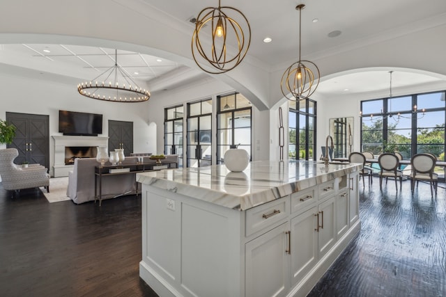 kitchen with a center island with sink, hanging light fixtures, light stone counters, a chandelier, and white cabinetry