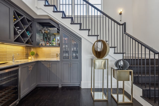 bar with light stone counters, a towering ceiling, beverage cooler, gray cabinets, and dark hardwood / wood-style floors