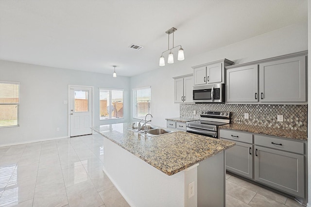 kitchen featuring a kitchen island with sink, gray cabinetry, stainless steel appliances, sink, and pendant lighting