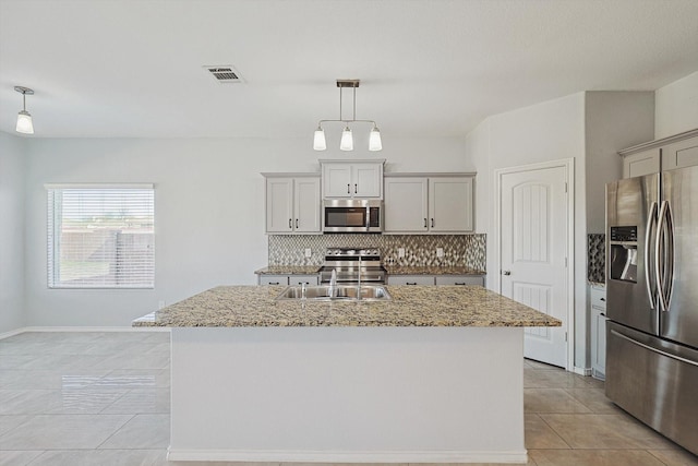 kitchen featuring a center island with sink, gray cabinets, stainless steel appliances, and decorative light fixtures