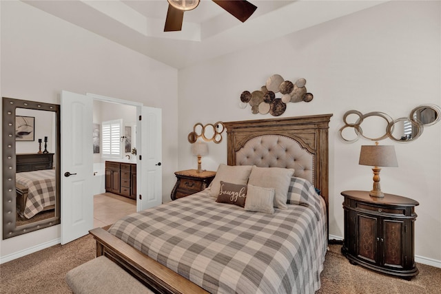 bedroom featuring light carpet, a ceiling fan, baseboards, a tray ceiling, and ensuite bath