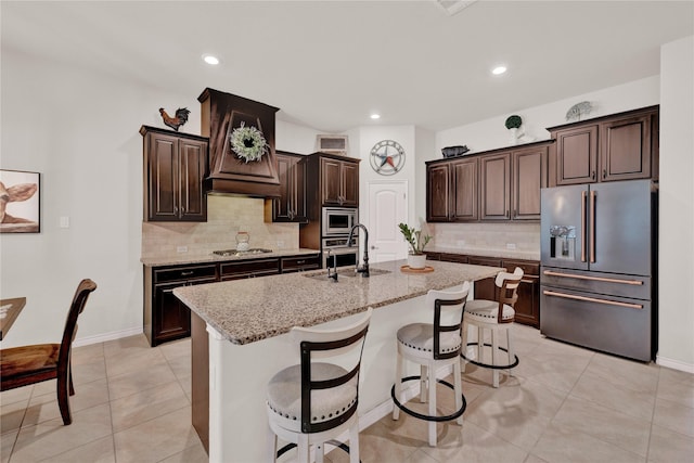 kitchen featuring a kitchen island with sink, appliances with stainless steel finishes, light stone counters, and a sink