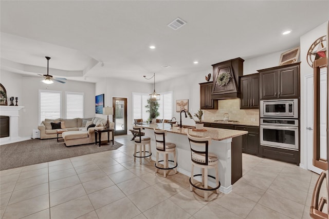 kitchen featuring stainless steel appliances, visible vents, open floor plan, a kitchen island with sink, and a kitchen breakfast bar