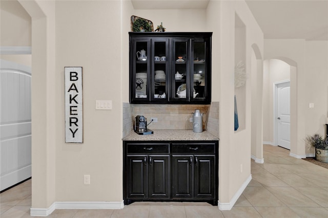 bar with arched walkways, baseboards, decorative backsplash, and light tile patterned floors