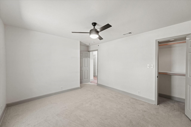 unfurnished bedroom with light carpet, a spacious closet, ceiling fan, and a closet