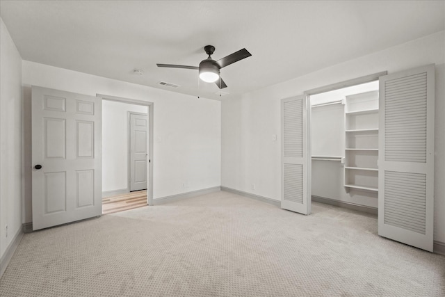 unfurnished bedroom with ceiling fan, a closet, a walk in closet, and light colored carpet