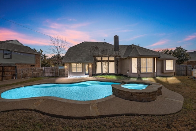 pool at dusk featuring a fenced backyard and a pool with connected hot tub