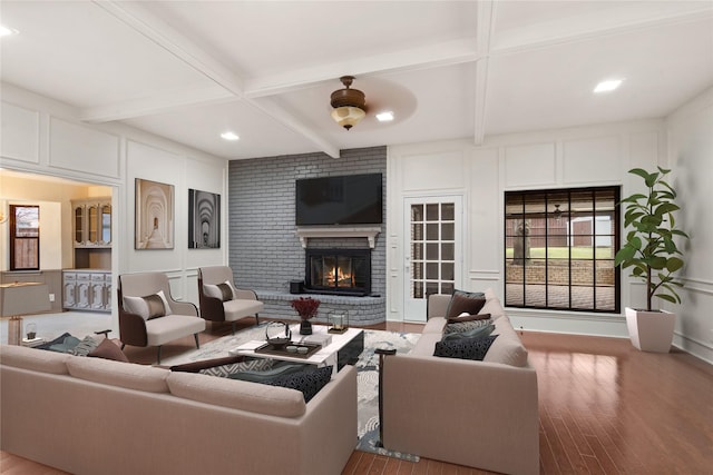 living room with a brick fireplace, beamed ceiling, and hardwood / wood-style floors