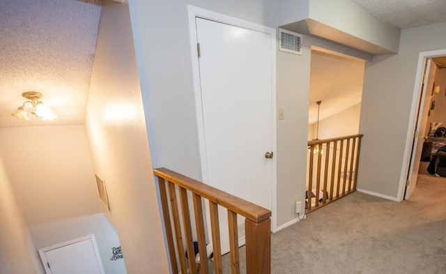 corridor with a textured ceiling and light colored carpet