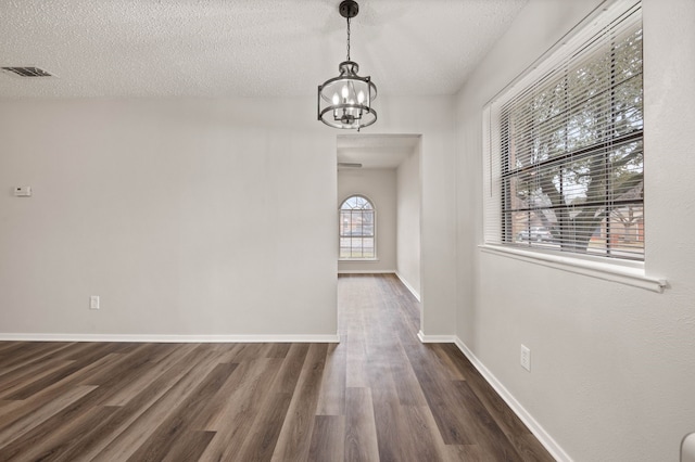 unfurnished dining area with a textured ceiling, baseboards, dark wood finished floors, and a notable chandelier