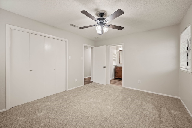 unfurnished bedroom with a textured ceiling, ensuite bathroom, carpet floors, visible vents, and a closet