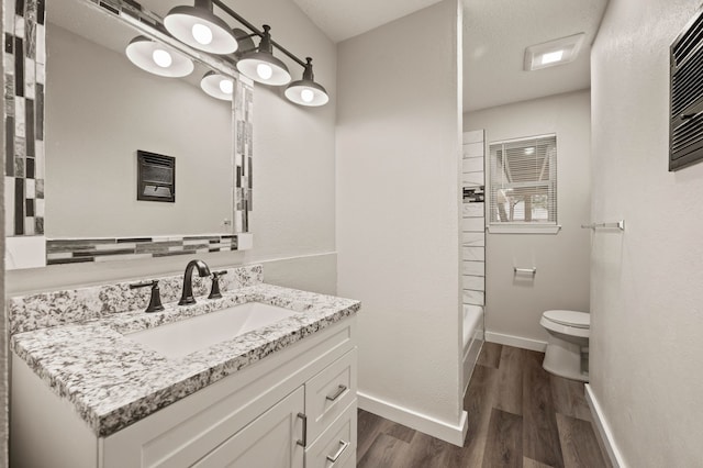 bathroom with toilet, wood finished floors, vanity, baseboards, and shower / washtub combination