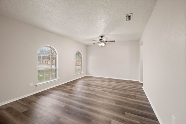 spare room featuring a ceiling fan, visible vents, dark wood finished floors, and baseboards