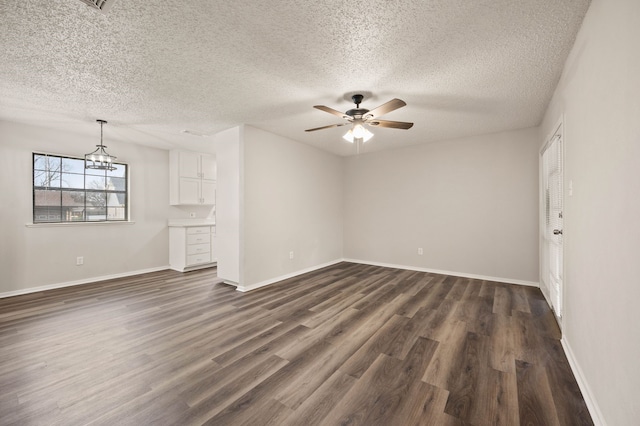 unfurnished living room with dark wood finished floors, a textured ceiling, baseboards, and ceiling fan with notable chandelier