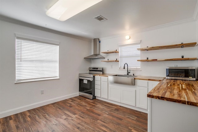 kitchen with butcher block counters, wall chimney exhaust hood, stainless steel appliances, sink, and white cabinetry