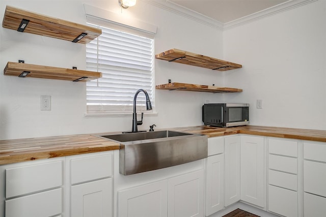 kitchen featuring white cabinets, crown molding, butcher block countertops, and sink