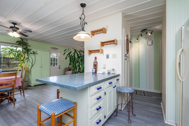 kitchen featuring a breakfast bar, decorative light fixtures, white refrigerator, kitchen peninsula, and white cabinets