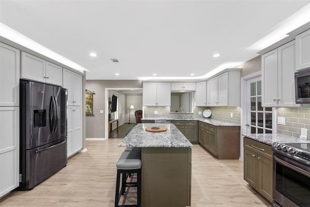 kitchen featuring appliances with stainless steel finishes, light stone countertops, a center island, gray cabinets, and sink