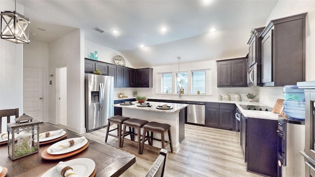 kitchen featuring appliances with stainless steel finishes, a kitchen breakfast bar, decorative light fixtures, a kitchen island, and light wood-type flooring