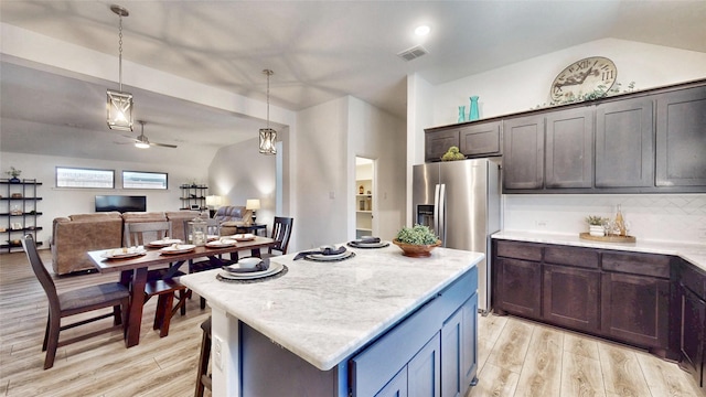 kitchen with light wood-type flooring, hanging light fixtures, a kitchen island, light stone countertops, and dark brown cabinets