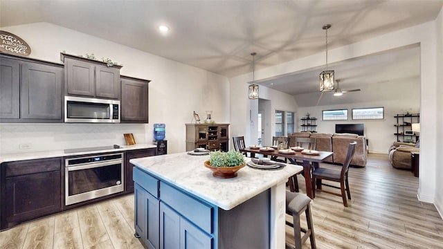 kitchen with hanging light fixtures, stainless steel appliances, a center island, light hardwood / wood-style floors, and dark brown cabinets