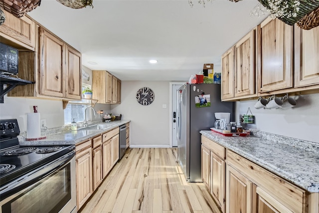 kitchen with appliances with stainless steel finishes, light brown cabinetry, light stone counters, light hardwood / wood-style floors, and sink