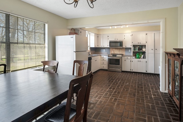 kitchen featuring a notable chandelier, stainless steel appliances, white cabinetry, and a textured ceiling