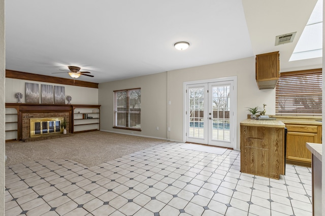 unfurnished living room featuring light carpet, french doors, ceiling fan, and a fireplace