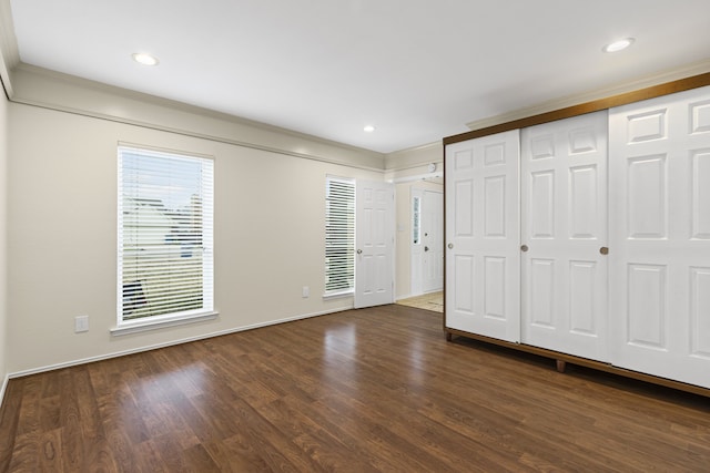 unfurnished bedroom with dark wood-type flooring, crown molding, and a closet